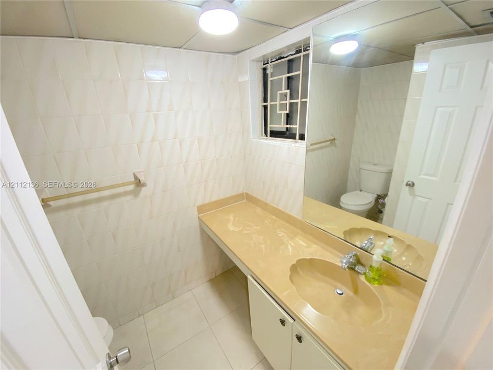 Bathroom featuring light-toned tile wall cladding, a molded vanity countertop with integrated scalloped sink, a full-width vanity mirror, and white shaker-style cabinetry