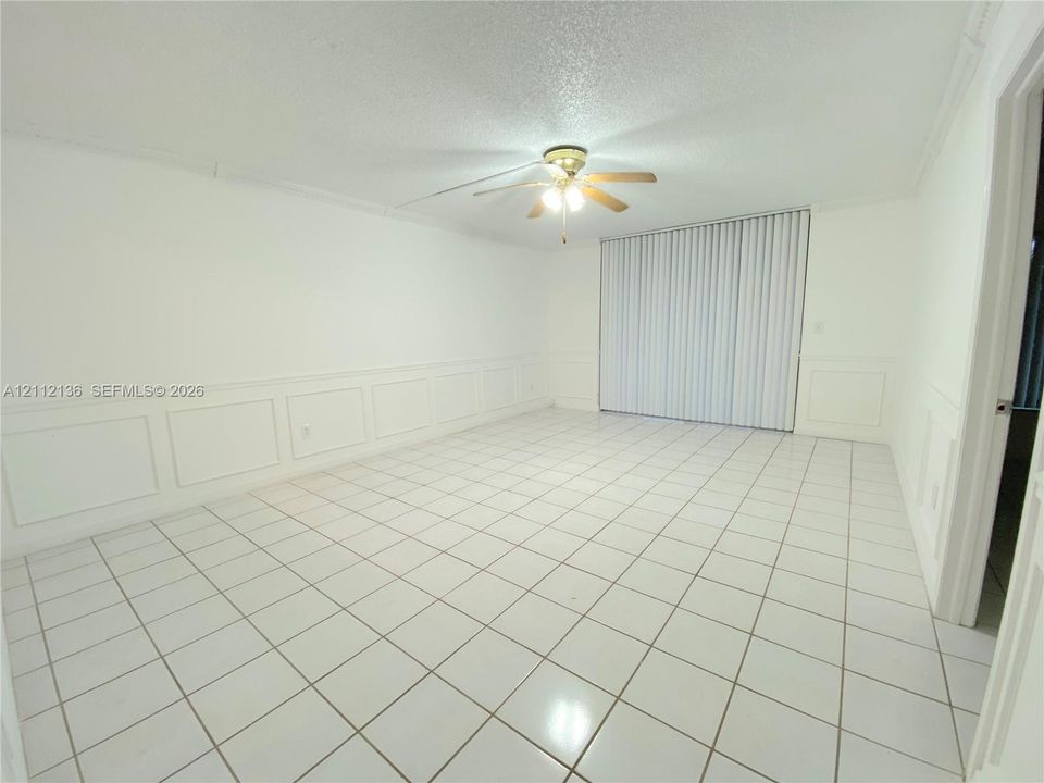 Interior space featuring tile flooring, wall wainscoting, a ceiling fan with light fixture, and vertical window blinds