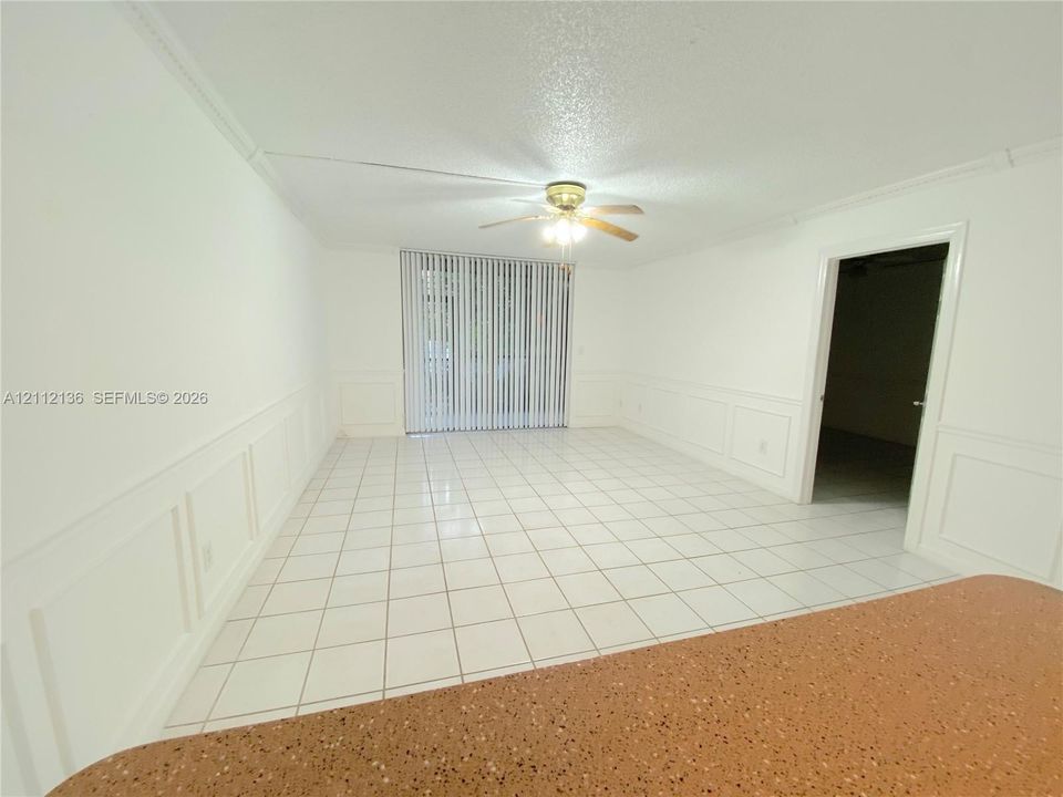 Interior area featuring white tile flooring, white wainscoting, a ceiling fan with integrated lighting, and sliding glass doors with vertical blinds