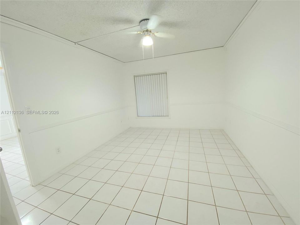 Room featuring light-colored tile flooring, wall-mounted wainscoting, and a ceiling-mounted light fixture with a fan