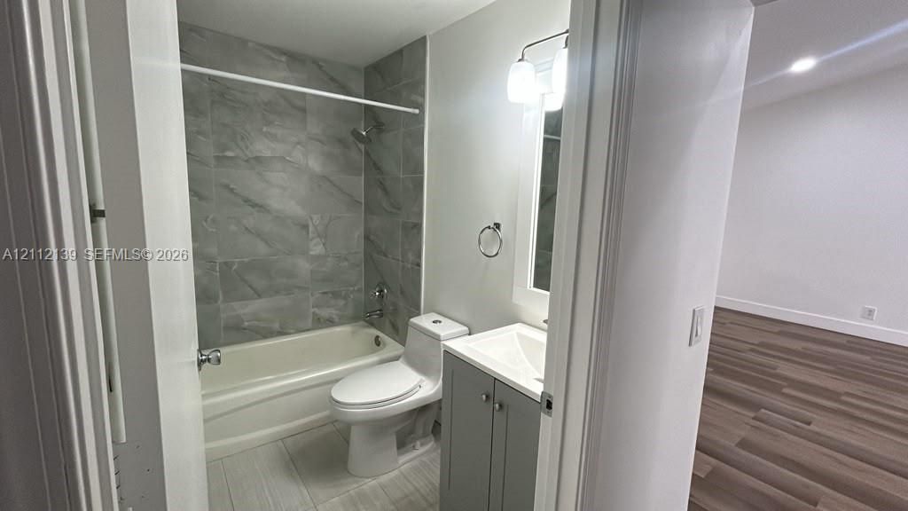 Bathroom featuring a gray vanity cabinet with a white integrated sink, porcelain tile tub surround with a metallic shower fixture, and light-toned tile flooring