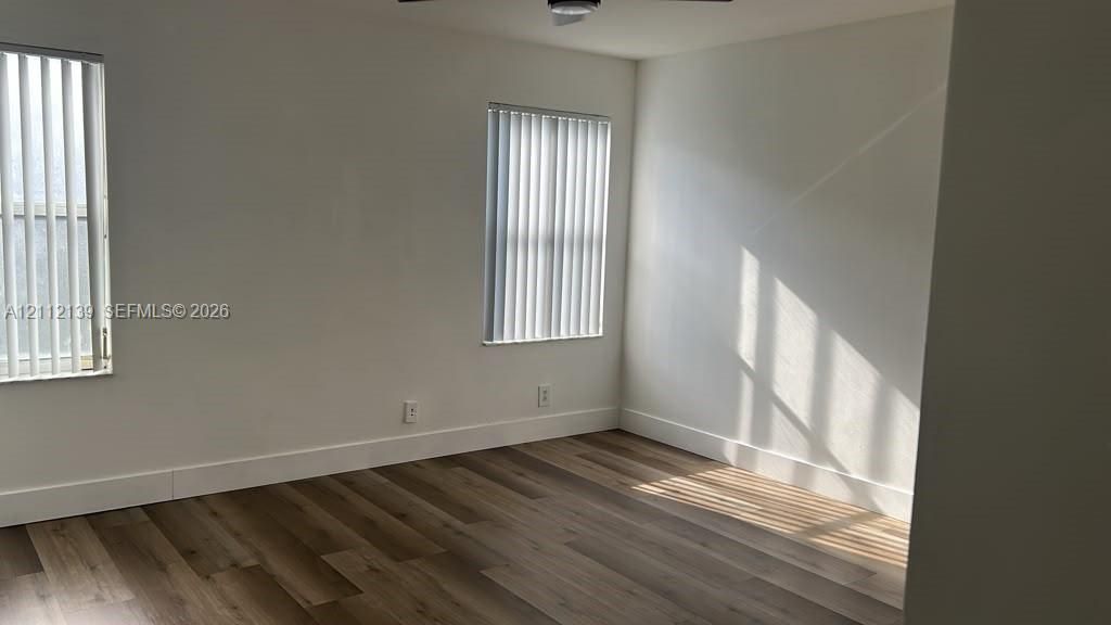 Neutral interior space featuring wood-finish flooring, white walls, and vertical window blinds