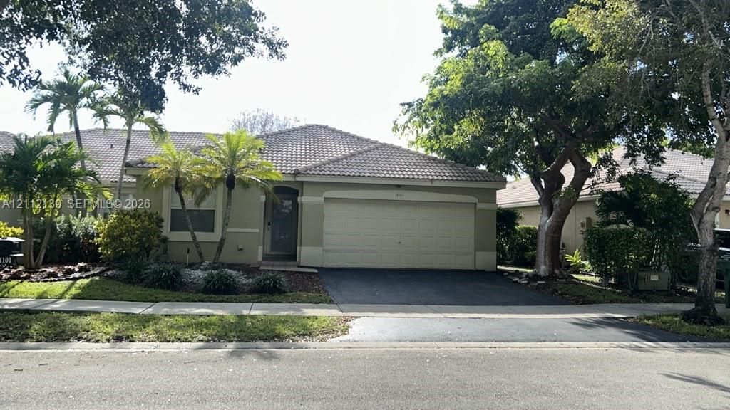 Stucco exterior featuring a tiled roof, attached two-car garage, paved driveway, and mature landscaping
