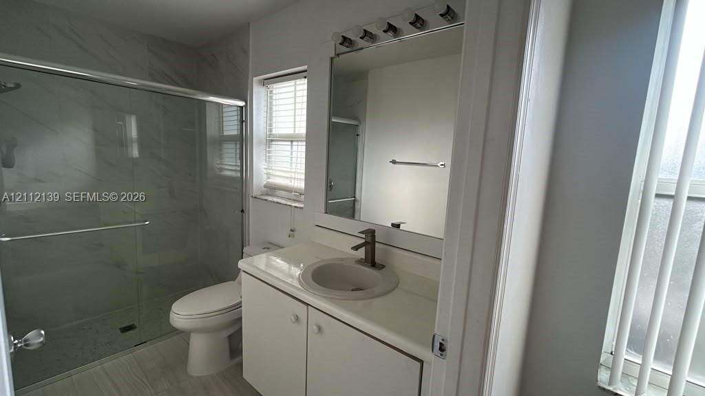 Bathroom featuring a stone-look countertop with an integrated basin, wall-mounted mirror, glass-enclosed shower with tiled surround, and metal faucet fixtures