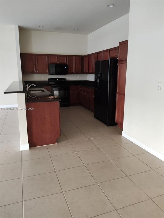Kitchen featuring dark wood cabinetry, contrasting stone-finish countertops, black built-in appliances, recessed lighting, and tile flooring