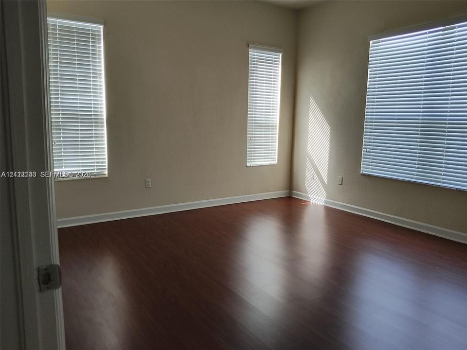 Room featuring wood-finish flooring, neutral wall paint, and three windows equipped with horizontal blinds