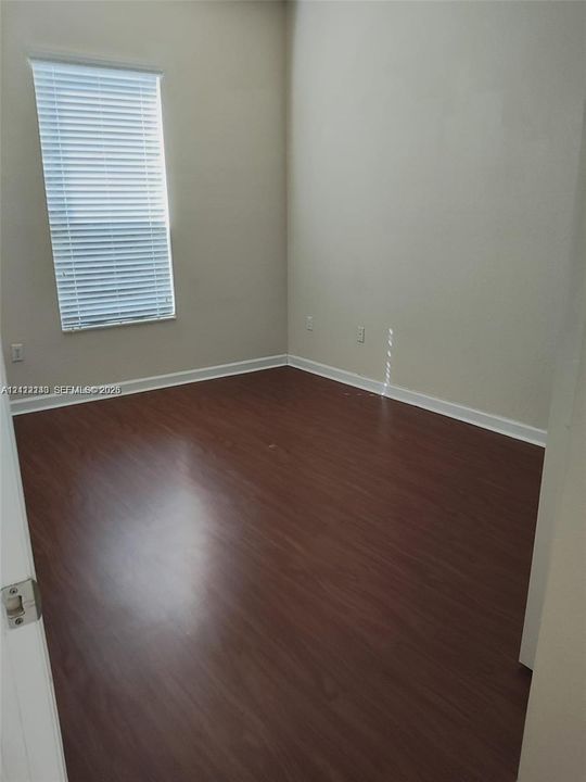 Interior room featuring wood-finish flooring, neutral wall tones, and a window equipped with horizontal blinds