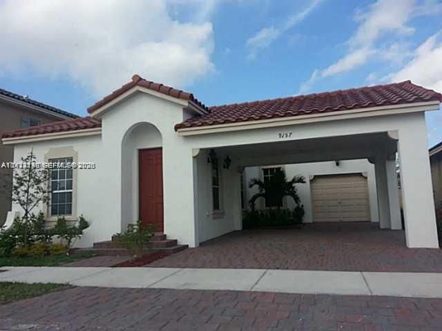 Stucco exterior featuring a tiled roof, arched entryway, brick-paver driveway, and an attached carport with an integrated garage door