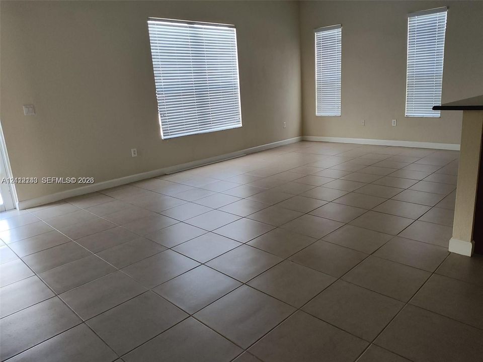 Neutral-toned ceramic tile flooring, three large windows with horizontal blinds, and smooth-finish walls