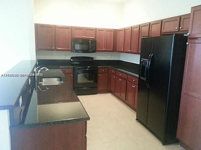 Kitchen featuring dark-toned cabinetry, solid-surface countertops, black appliances, and a stainless steel under-mount sink with a chrome finish faucet