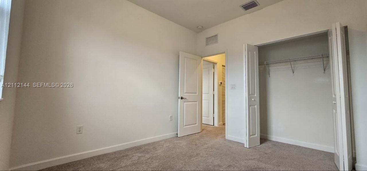 Room featuring neutral-toned carpeting, two-panel interior doors, and a reach-in closet with integrated wire shelving