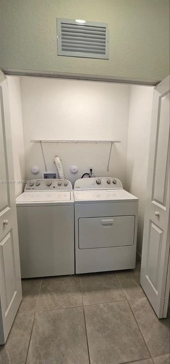 Laundry closet featuring large-format tile flooring, white bi-fold doors, and a built-in wire shelving rack