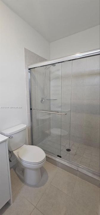 Walk-in shower with sliding glass doors, tiled surround, and integrated seating, featuring large-format floor tiling and a high-profile toilet