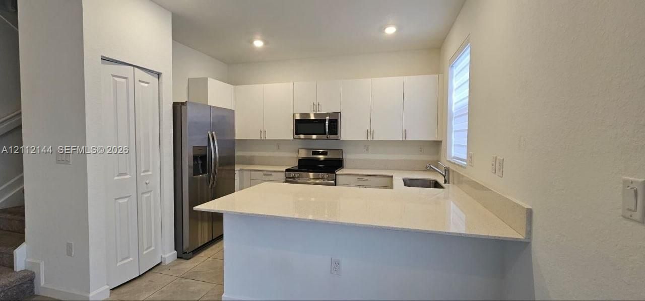 Kitchen featuring white cabinetry, solid-surface countertops, stainless steel appliances, and tile flooring