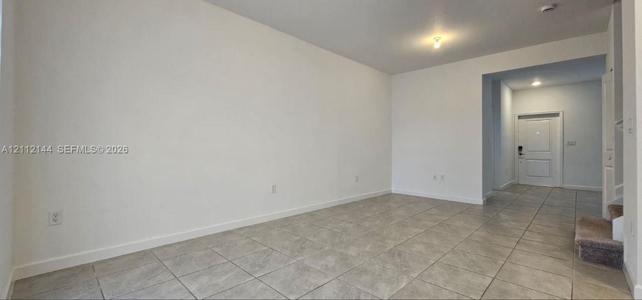 Neutral-toned interior featuring large-format ceramic tile flooring, clean-finished walls, flush-mount ceiling lighting, and a paneled entry door