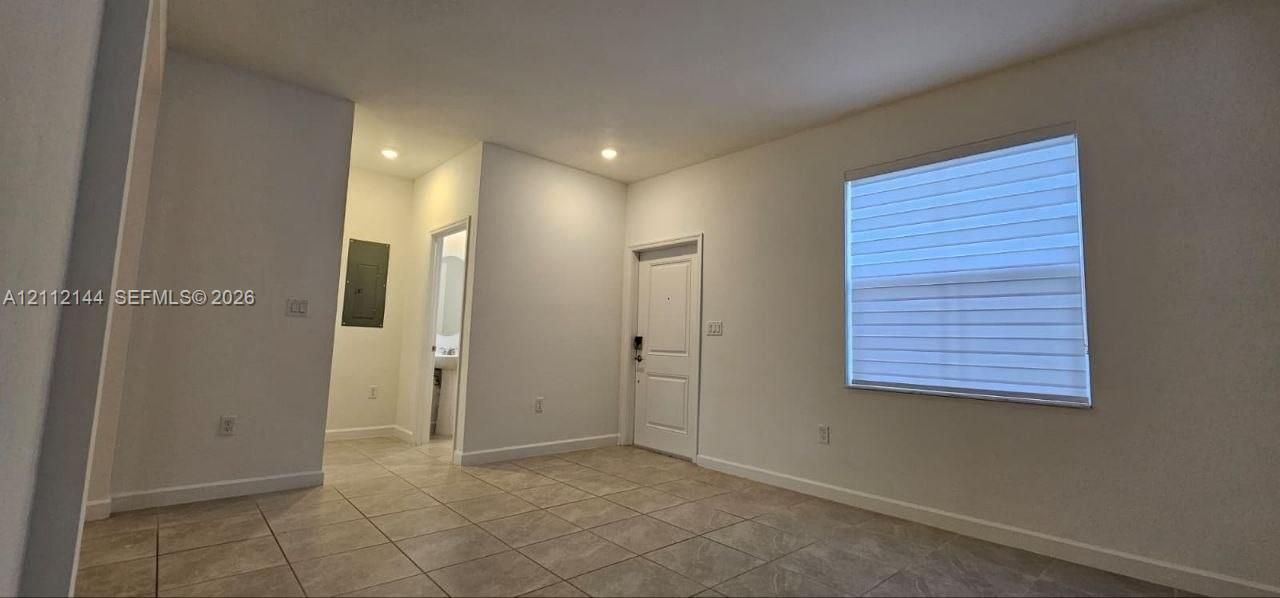 Interior space featuring neutral wall paint, tile flooring, recessed ceiling lighting, a solid-panel door, and a horizontal-slat window shade