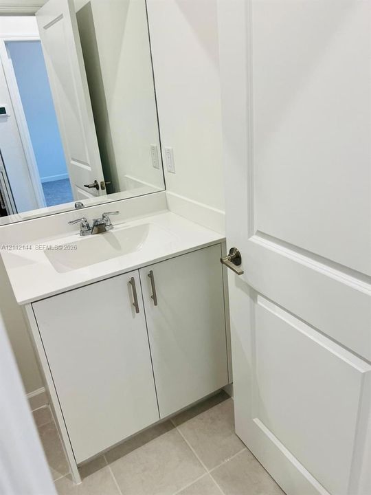 Bathroom vanity featuring a solid-surface countertop, an integrated sink, polished chrome faucet, white cabinetry with brushed nickel pulls, and a wall-mounted mirror