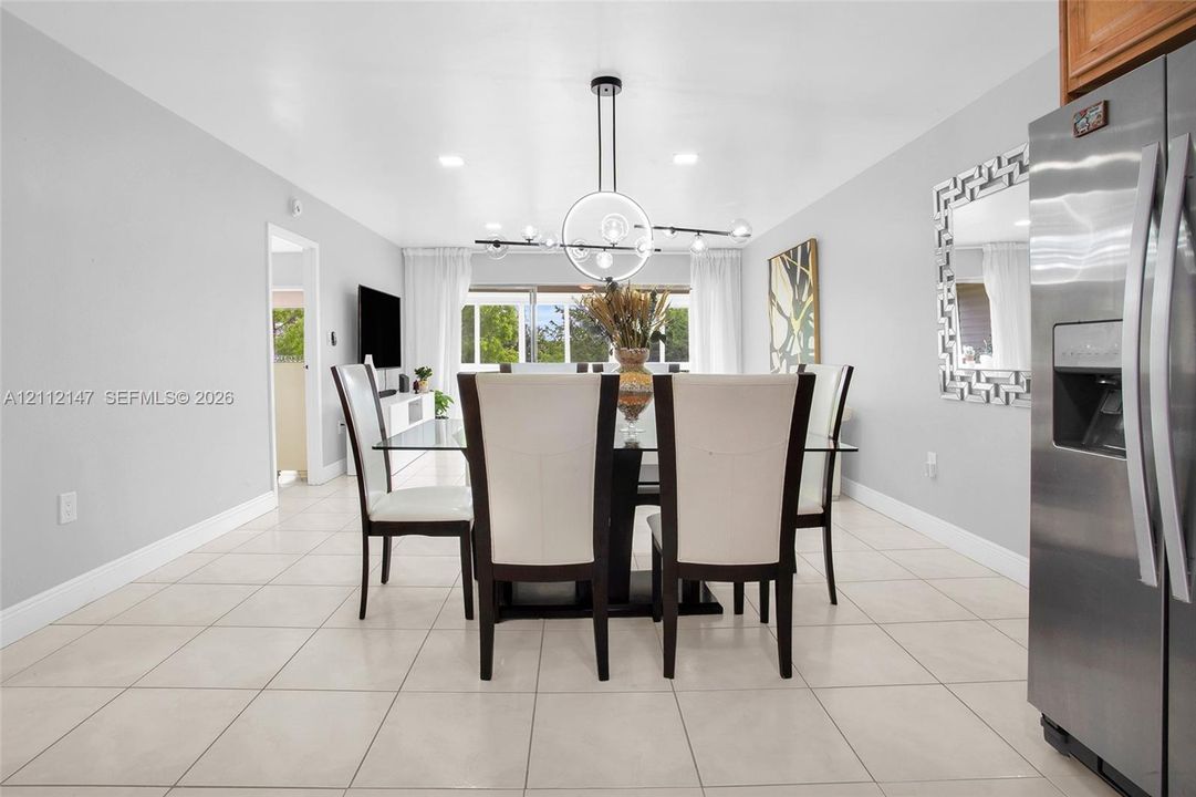 Dining area featuring large-format tile flooring, a geometric multi-light pendant fixture, recessed ceiling lighting, and a stainless steel side-by-side refrigerator