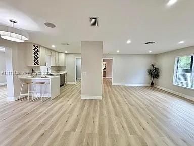 Open-concept interior featuring wood-finish flooring, a kitchen peninsula with integrated seating, built-in wine storage, recessed lighting, and a modern drum pendant fixture