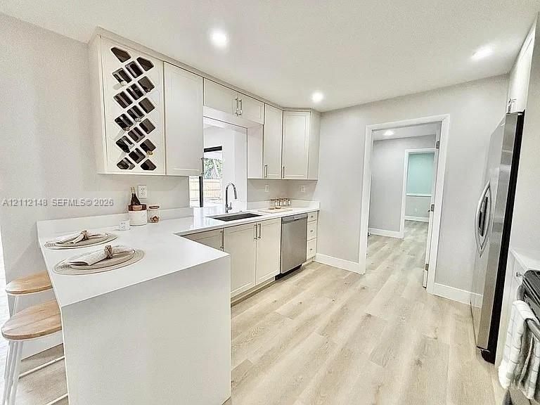 Kitchen featuring white Shaker-style cabinetry with integrated wine rack, solid-surface countertops, stainless steel appliances, and wood-finish flooring