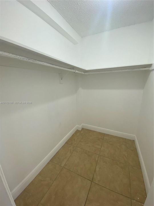 Walk-in storage space featuring ceramic tile flooring, built-in shelving, and a mounted hanging rod