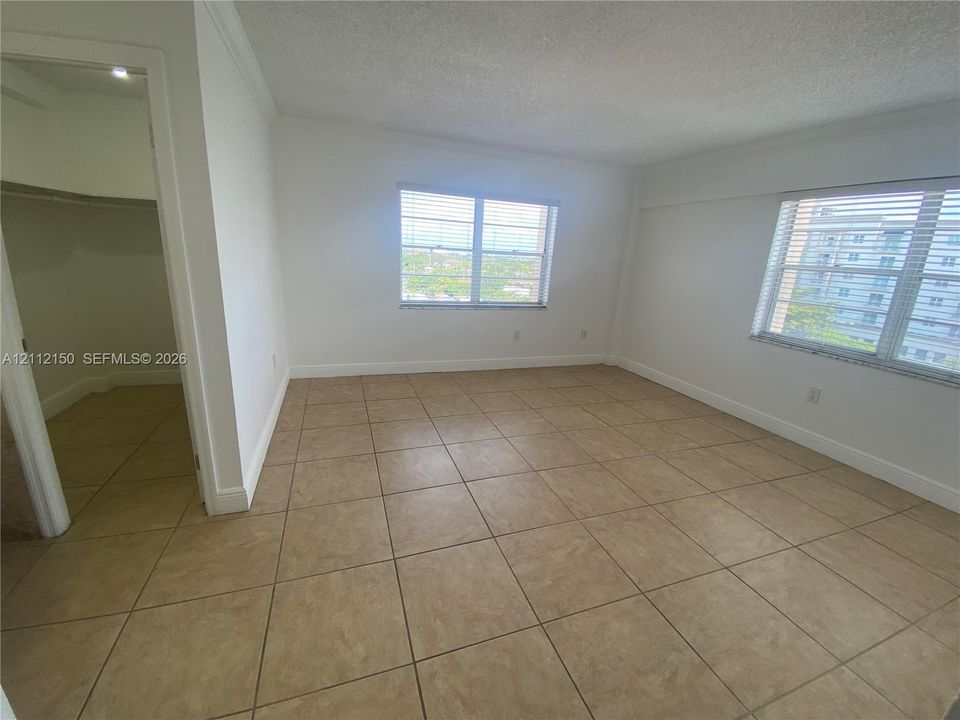 Neutral interior space featuring large-format tile flooring, textured ceilings, dual windows with horizontal blinds, and a built-in walk-in closet