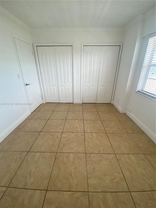 Neutral-toned tile flooring, dual bi-fold closets, and a window with horizontal blinds