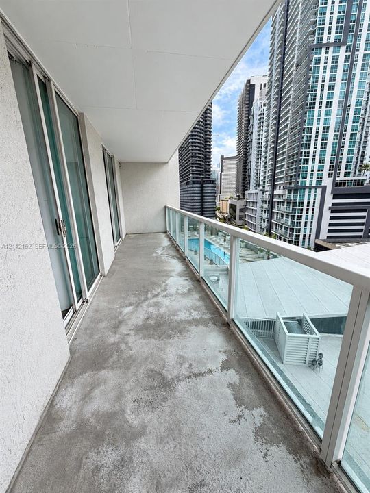 Covered balcony featuring a glass panel railing, concrete flooring, and sliding glass door access
