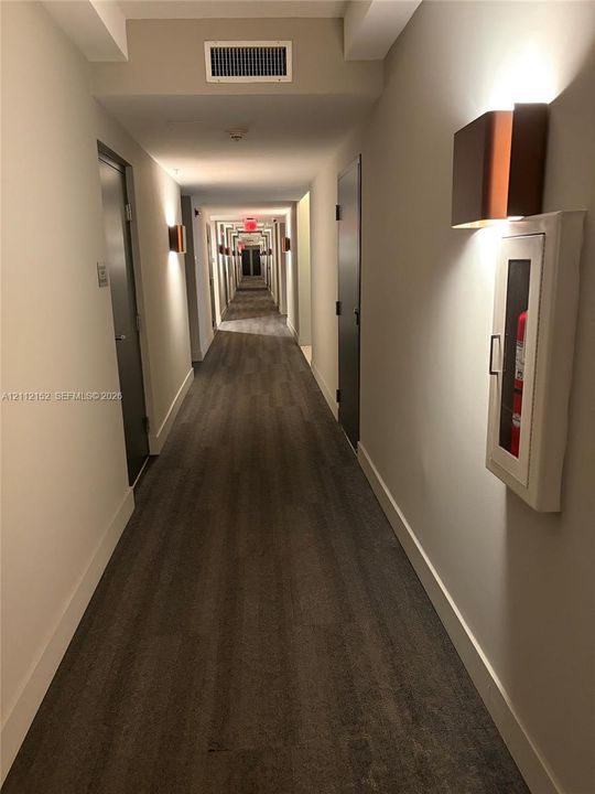 Hallway featuring wood-finish flooring, neutral wall tones, and architectural wall-mounted sconces