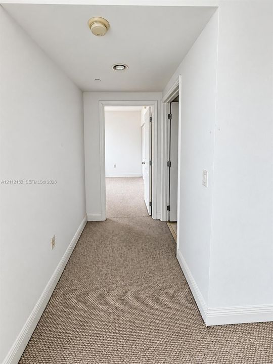 Hallway featuring neutral wall-to-wall carpeting, crisp white interior doors, and recessed ceiling lighting