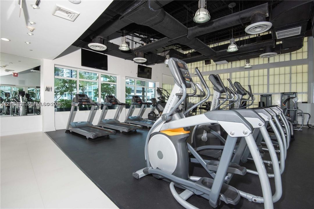 Fitness center featuring large-format windows, industrial-style exposed ceiling, recessed lighting, rubber flooring, and full-wall mirrors