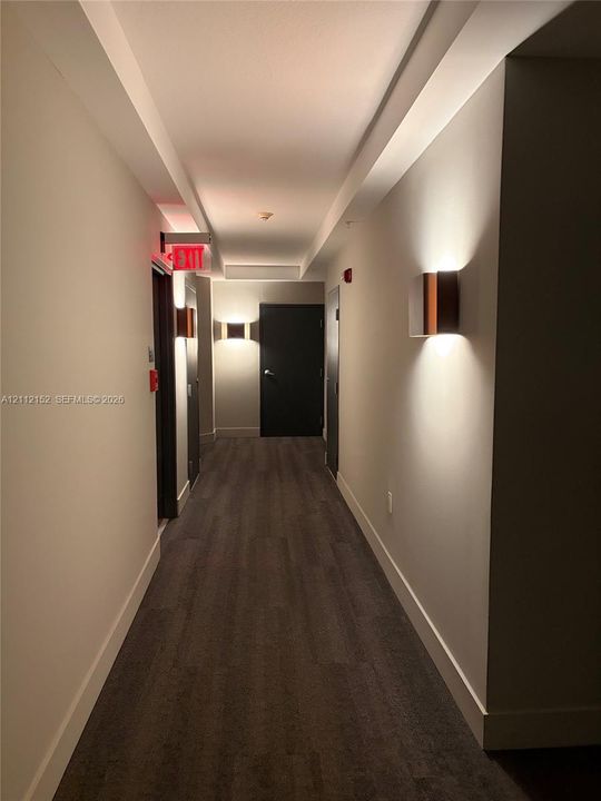 Hallway featuring wood-finish flooring, recessed ceiling lighting, and wall-mounted sconces