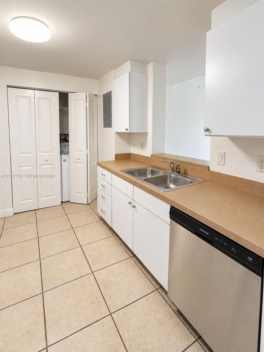 Kitchen featuring white shaker-style cabinetry, solid-surface countertops, stainless steel dual-basin sink, integrated stainless steel dishwasher, and ceramic tile flooring