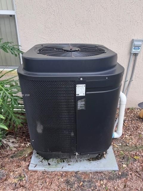 Exterior HVAC condenser unit featuring a black metal protective grill, solid casing, and reinforced base pad