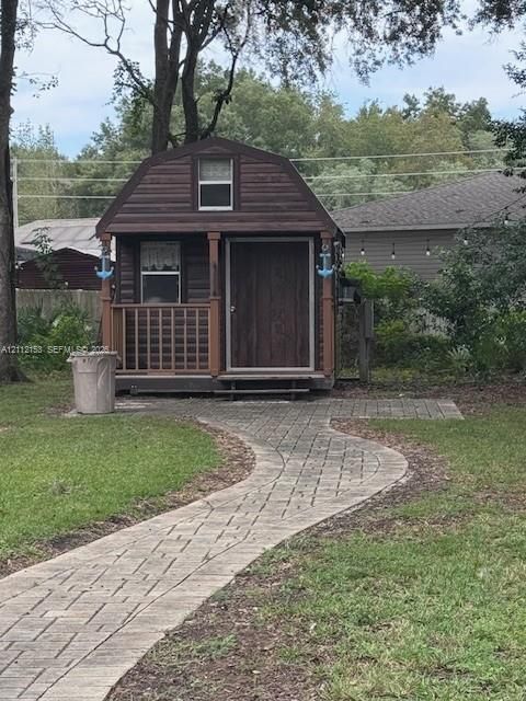 Detached outbuilding featuring wood-style siding, a gambrel roof, and a covered front porch with a lattice railing, complemented by a paver walkway