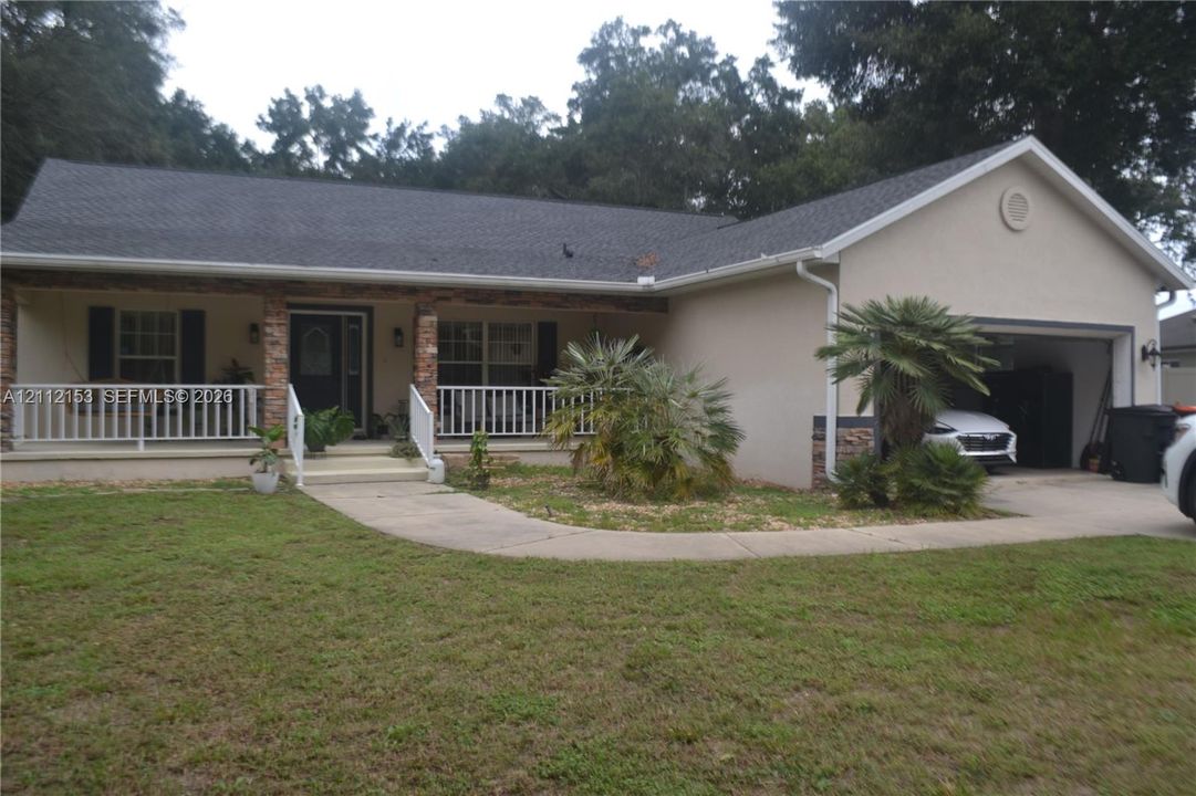 Single-story exterior featuring a covered front porch with stone-accented columns, a white railing, a concrete walkway, and an attached garage