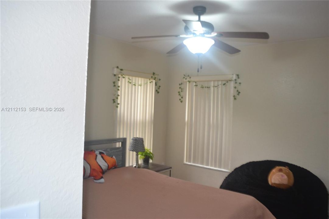 Neutral wall finish featuring two windows with vertical blinds and a ceiling-mounted light fixture with a fan