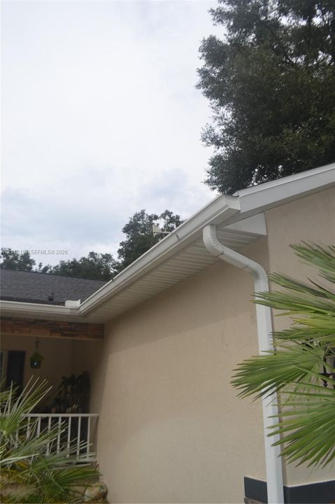 Stucco exterior featuring white-finished rain gutters, soffits, and fascia, complemented by stone-veneer accents and a white-railing porch