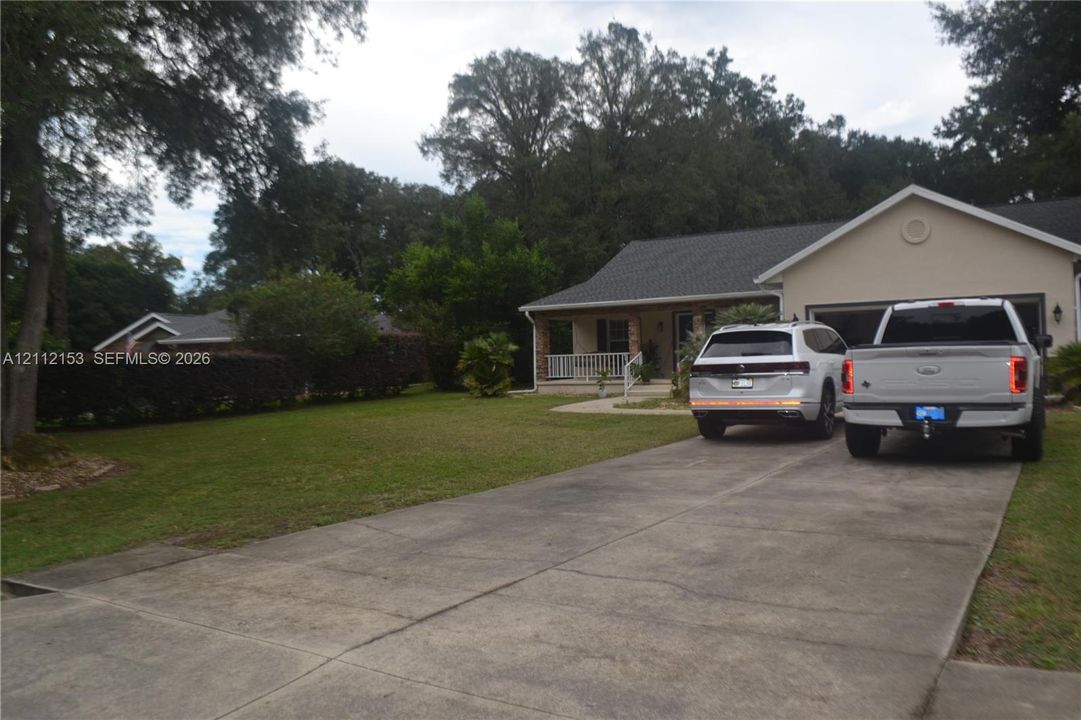 Single-story exterior featuring a concrete driveway, two-car garage, covered front porch, and mature landscaping
