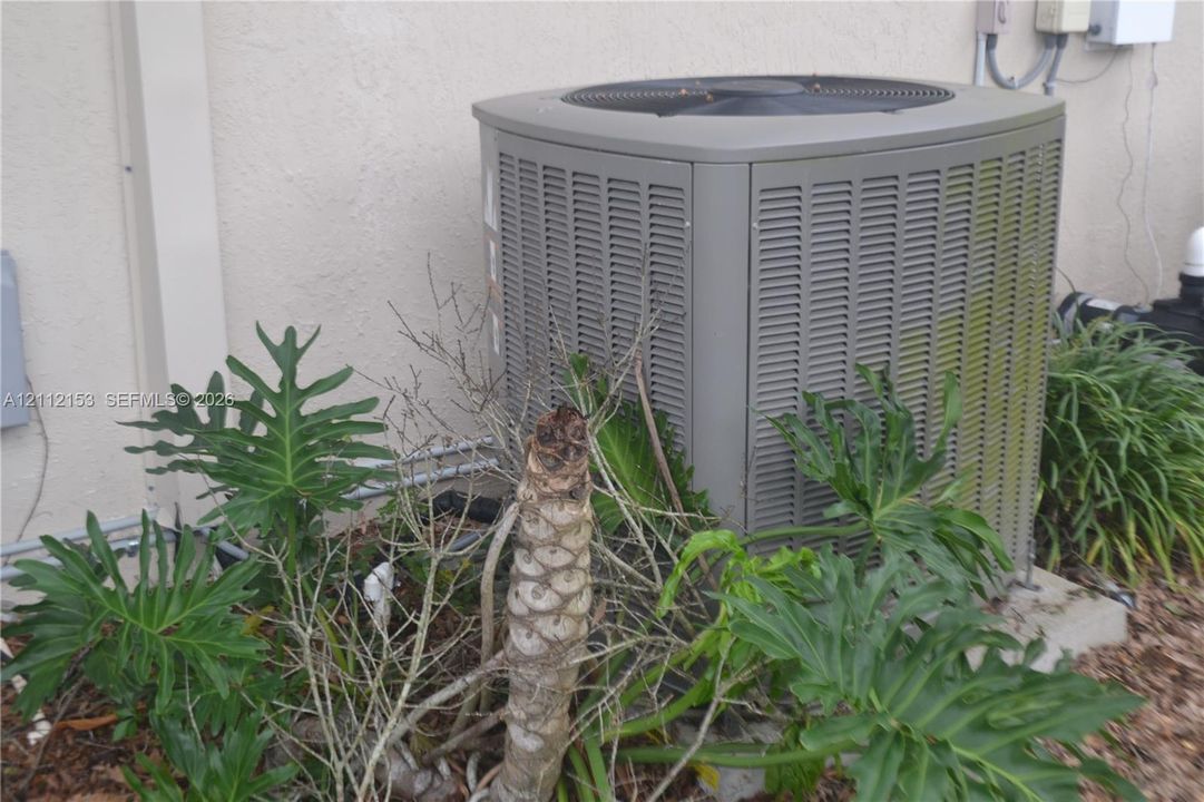 Exterior HVAC condenser unit mounted on a concrete pad with surrounding ornamental landscaping