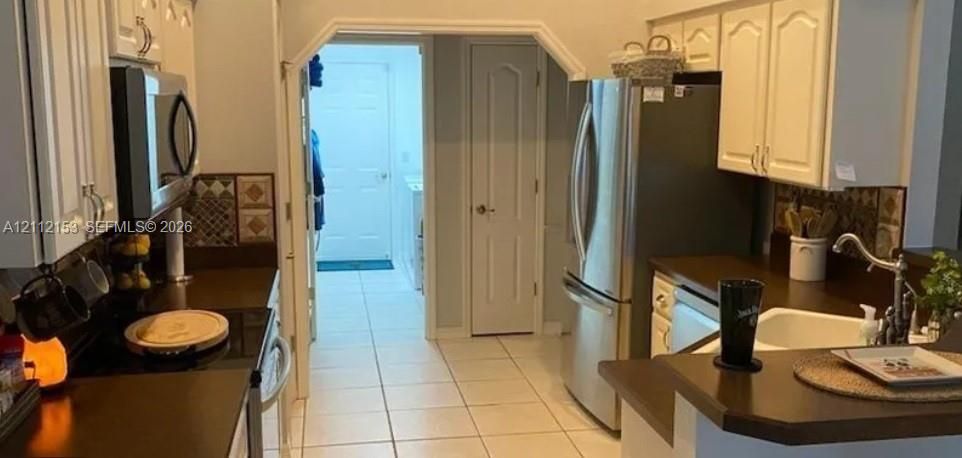 Kitchen featuring white shaker-style cabinetry, stainless steel refrigerator, built-in microwave, tiled backsplash, and solid-surface countertops