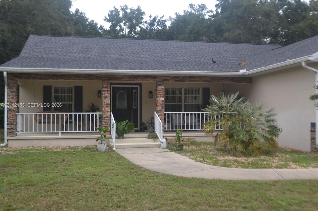 Exterior facade featuring stone veneer columns, a covered front porch, white railings, and a shingle roof