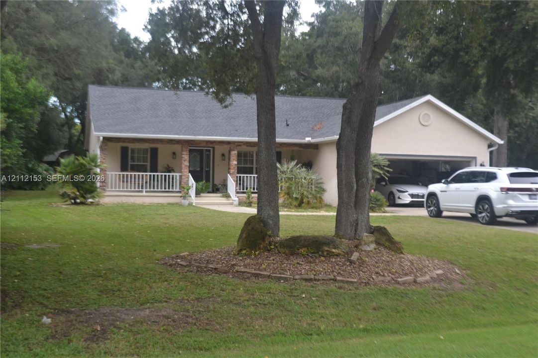 Single-story residence featuring a covered front porch, stone-accented pillars, two-car garage, and mature landscaping
