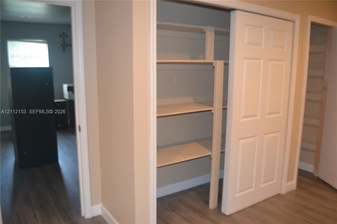 Interior storage closet featuring six-panel sliding doors and integrated wooden shelving, finished with wood-finish flooring