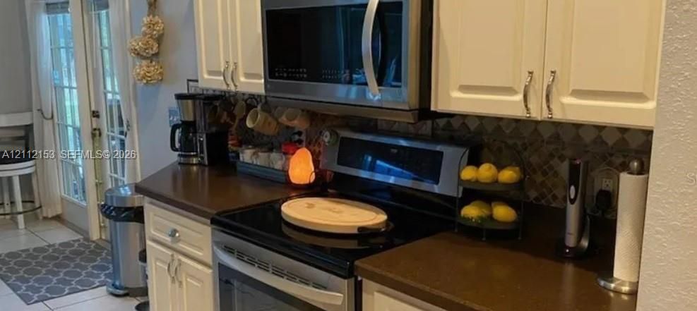 Kitchen featuring white cabinetry, solid-surface countertops, decorative stone tile backsplash, stainless steel over-the-range microwave, and glass-paned double doors