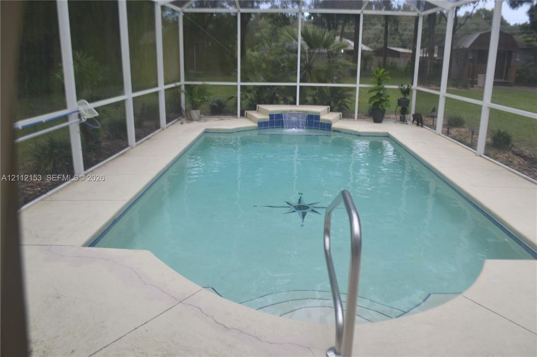 In-ground swimming pool featuring a compass rose mosaic inlay, water feature, concrete deck, and full-screen enclosure