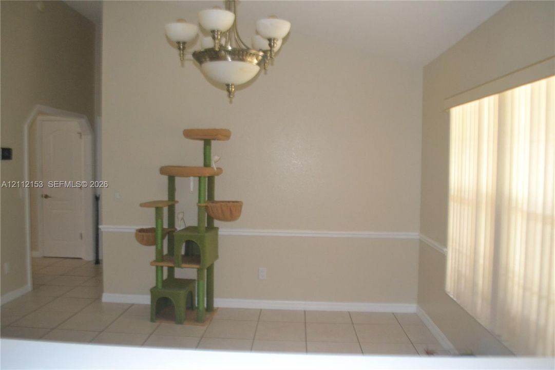Vaulted ceiling, decorative chandelier with glass shades, chair rail molding, and large-format tile flooring