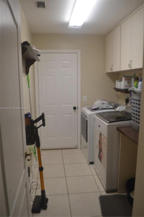 Laundry room featuring ceramic tile flooring, upper cabinetry, a solid-surface countertop, and overhead flush-mount lighting
