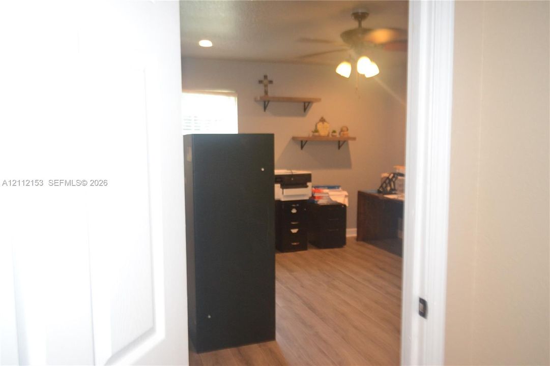 Room interior featuring wood-finish flooring, ceiling fan with integrated lighting, recessed lighting, and wall-mounted wooden shelving