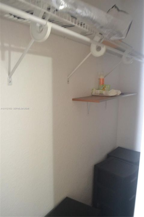 Storage area featuring a wall-mounted wire shelf with an integrated hanging rod and an additional wood-finish shelf